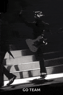 a man is playing a guitar on a stage in a black and white photo with a caption that says `` go team '' .