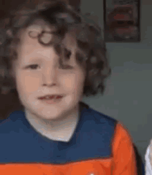 a young boy with curly hair is wearing a blue and orange striped shirt and making a funny face .