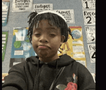 a young boy with dreadlocks is taking a selfie in front of a bulletin board .