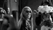 a woman wearing sunglasses and a black leather jacket is smiling in a black and white photo .