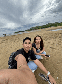 a man and a woman sit on a sandy beach looking at their cell phones