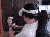 a man wearing an oculus headset is sitting in a chair holding a controller .