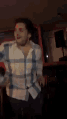 a man wearing a plaid shirt is dancing in a dark room .