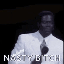 a man in a white suit and tie is standing in front of a microphone and saying nasty bitch .