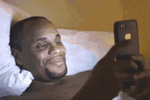 a shirtless man is laying in bed looking at a cell phone
