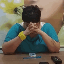 a woman is sitting at a table with her hands folded and a remote control .
