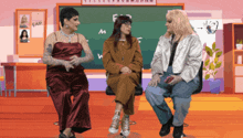 three women are sitting in front of a chalkboard that has the letter f on it