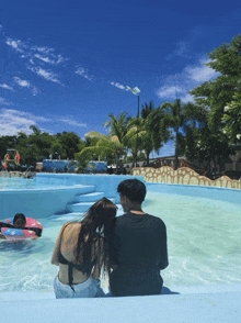 a man and a woman are sitting on the edge of a swimming pool