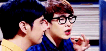 a man wearing glasses talks to another man in a blue shirt