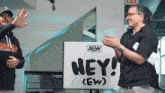 two men clapping in front of a sign that says hey