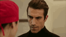a man and a woman are looking at each other in a room . the man is wearing a red hat .