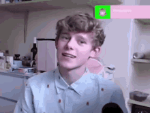 a young man with curly hair is sitting in a kitchen with a green screen in the background .
