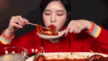 a woman in a red sweater is eating food with chopsticks from a bowl .