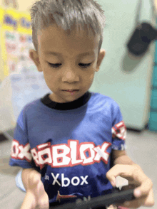 a young boy wearing a blue roblox shirt is playing a game
