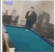 a man is standing in front of a pool table singing into a microphone .