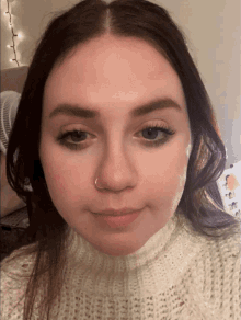 a woman wearing a white sweater with a nose ring