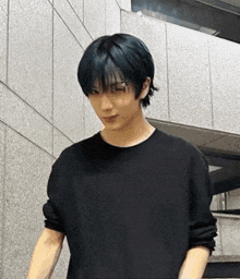 a young man with blue hair is standing in front of a building wearing a black sweater .