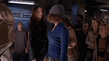 two women are standing next to each other and looking at the camera . one of the women is wearing a purple hat .
