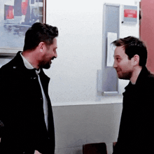 two men are standing next to each other in front of a wall