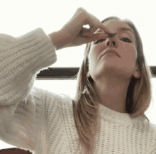 a woman in a white sweater is applying makeup to her eyes