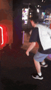 a man in a black shirt and blue shorts is dancing in front of a neon sign that says ' j ' on it