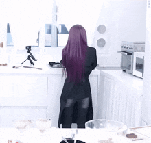 a woman with purple hair is standing in a white kitchen
