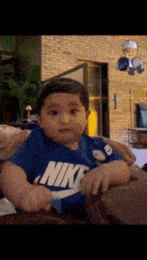 a baby wearing a blue nike shirt sitting on a couch