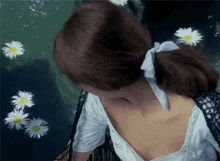 a woman in a white dress is standing in the water with daisies floating in the water .