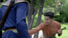 a man in a blue shirt is holding a sword and a man in a red shirt is holding a stick .