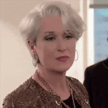 a woman with gray hair is wearing a gold jacket