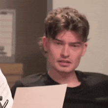 a young man is holding a piece of paper in his hand and making a funny face .