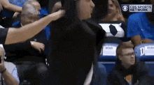 a referee is standing in the stands during a basketball game and talking to a player .