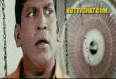a close up of a man 's face with a fan in the background and the website kuttychat.com in the corner