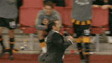 a man in a suit and tie is running on a soccer field with other players