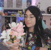 a woman wearing headphones holds a bouquet of pink and white flowers in front of a sign that says renrize