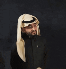 a man with a beard wears a black jacket and a white head scarf