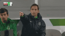 a man wearing a nike jacket sits next to a man wearing a green jacket