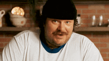 a man with a beard and mustache wearing a black hat and a white shirt