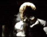 a man in a white jacket and tie is singing into a microphone in the dark .