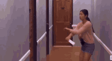 a woman in a pink shirt is running down a hallway with a pink light coming out of the door .