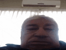a man with his eyes closed stands in front of a window with an air conditioner on the ceiling