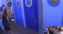 a woman in a black dress is standing in a room with blue doors