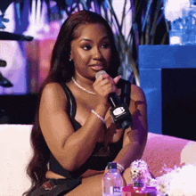 a woman is sitting on a couch holding a microphone with a bottle of aquafina water in front of her