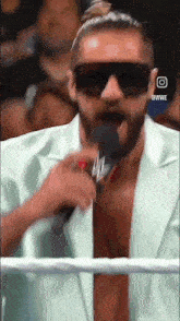 a man wearing sunglasses is speaking into a microphone while wearing a white suit and tie