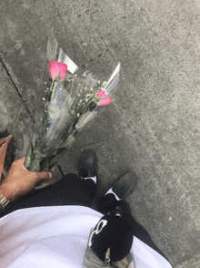 a person holding a bouquet of pink and white roses on the sidewalk
