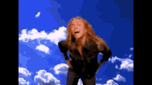 a woman stands in front of a blue sky with white clouds