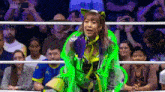 a woman in a green outfit is standing in a wrestling ring in front of a crowd of people .