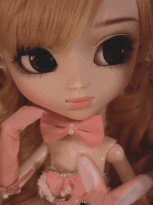 a close up of a doll wearing pink gloves and a pink bow