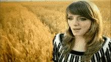 a woman in a striped shirt is standing in a field of tall grass