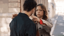 a man and a woman are standing next to each other on a street and the woman is putting her hand on the man .